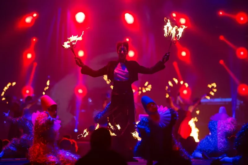 Groupe d’artistes levant des torches enflammées sous des projecteurs rouges pendant le spectacle Variations sur la flamme.