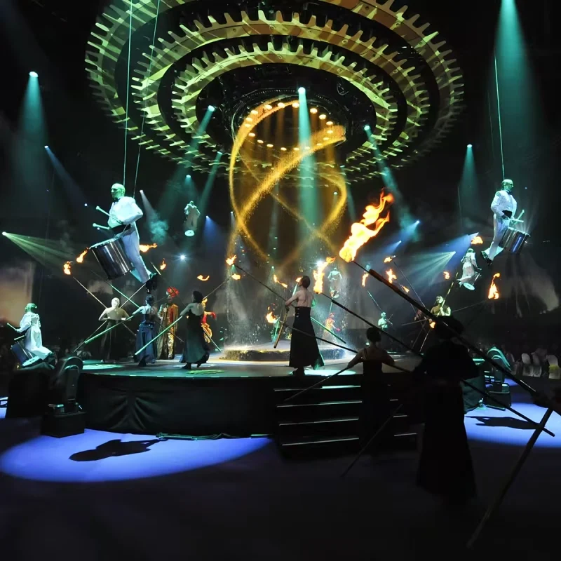 Artistes sur scène avec torches enflammées, arc lumineux et décor circulaire pendant Variations sur la flamme.