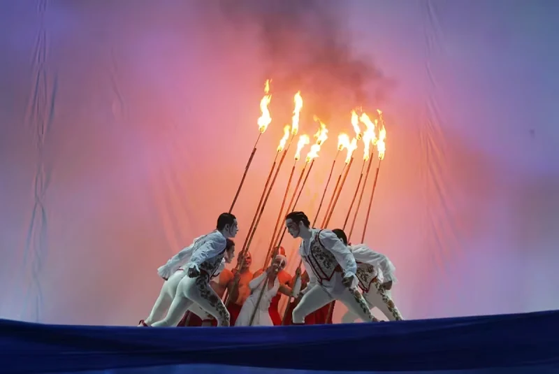 Trois artistes agenouillés portant de longues torches enflammées dans une scène chorégraphiée de Variations sur la flamme.