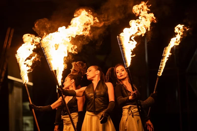 Trois artistes du spectacle Eden tenant des torches enflammées dans une scène nocturne spectaculaire.