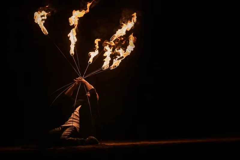 Artiste manipulant plusieurs torches enflammées en éventail sur une scène noire pendant le spectacle Horizons.