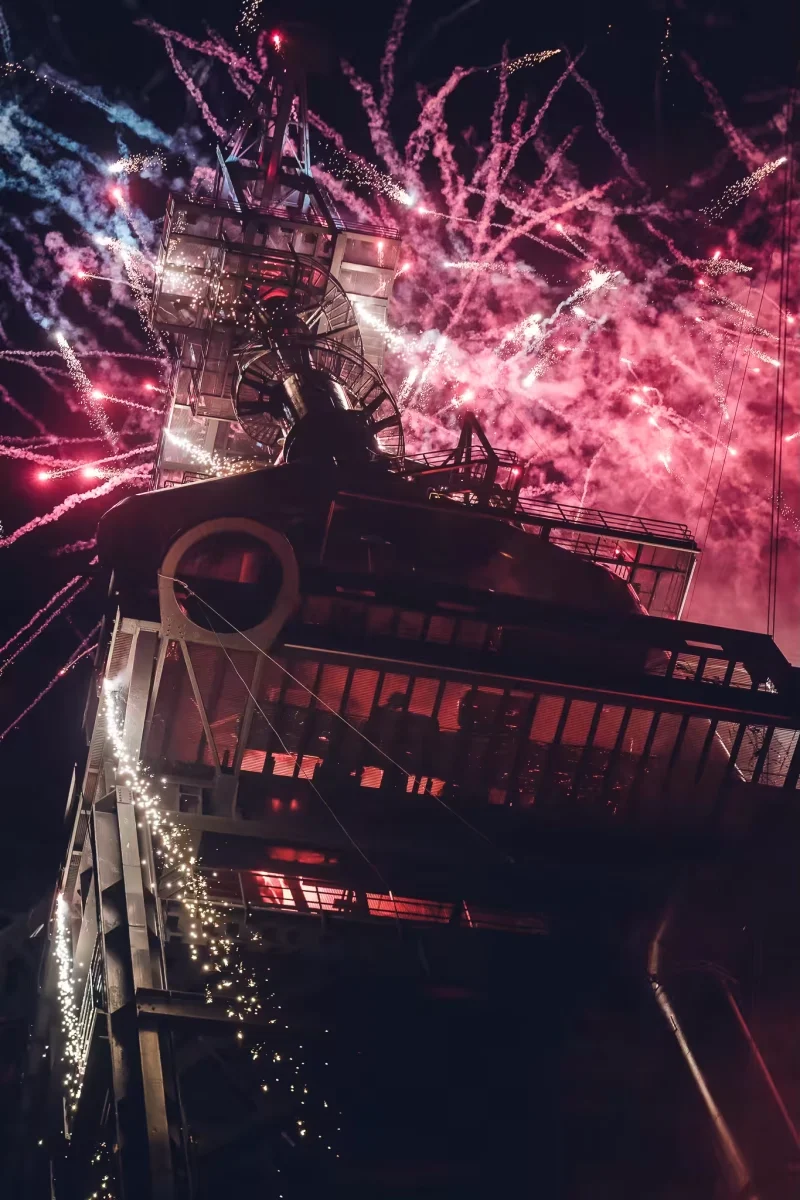 Feux d’artifice rouges et blancs éclatant au-dessus d’une structure industrielle pendant le final du spectacle Horizons.