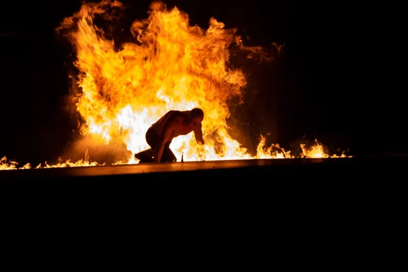 Artiste courbé au sol devant un grand rideau de flammes pendant une scène intense du spectacle Merveilles.