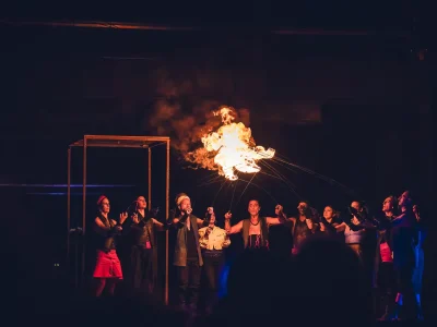Chœur d’artistes sur scène devant une grande flamme suspendue pendant le spectacle Y’a d’la joie.